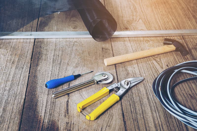 Geräte zum Verlegen von Klick Vinyl: Hammer, Cuttermesser, Bohrschrauber und Schneidelineal.